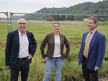 ÖDP-Stadtrat Dr. Stefan Müller-Kroehling, ÖDP Direktkandidat Lorenz Heilmeier und Landeschefin Agnes Becker vor einem Bauzaun, am Rande der Ochsenau